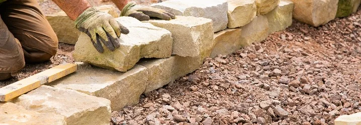 Person baut eine Trockenmauer aus Natursteinen.